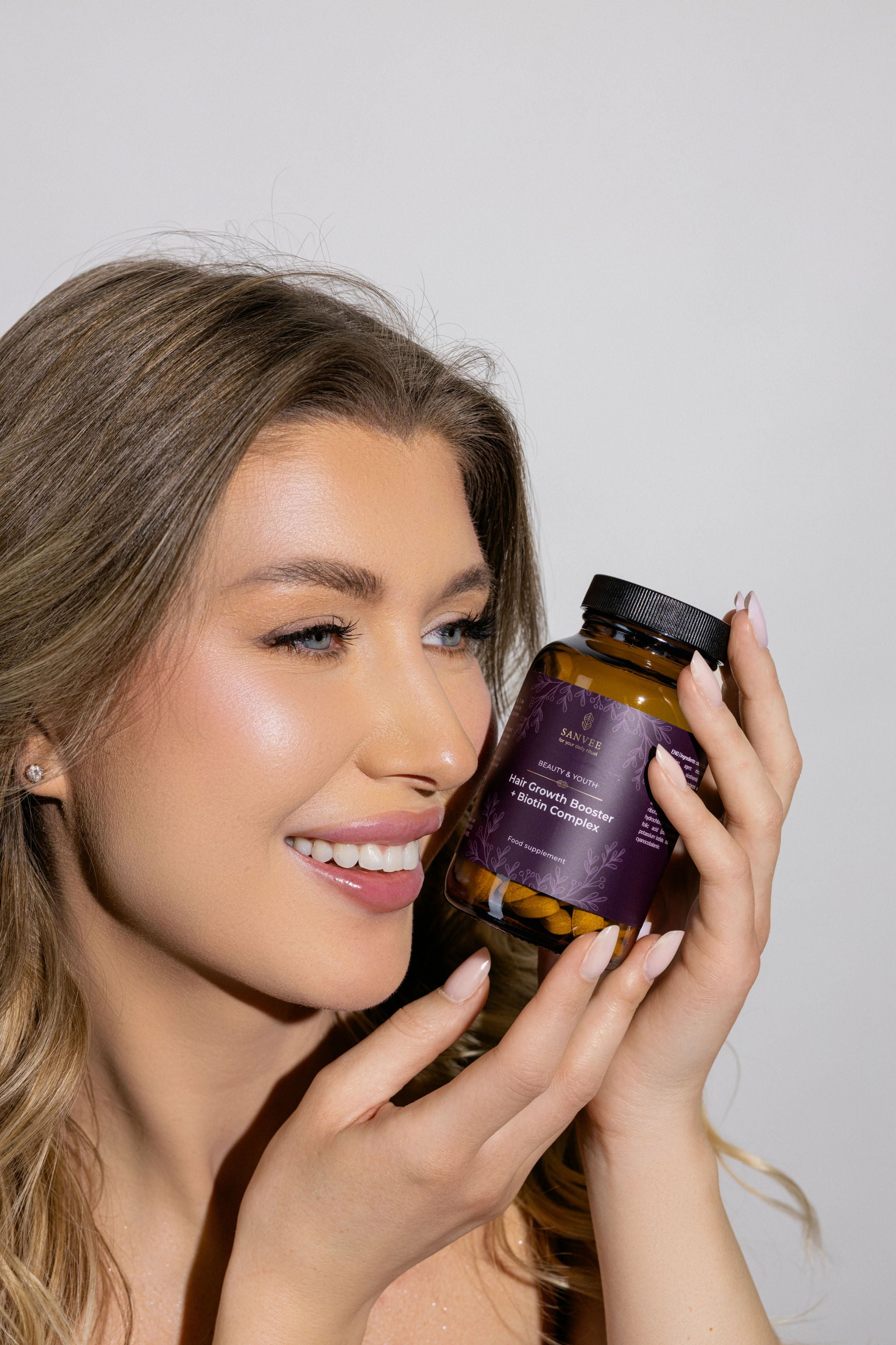 Woman holding Sanvee hair growth booster with biotin complex near face